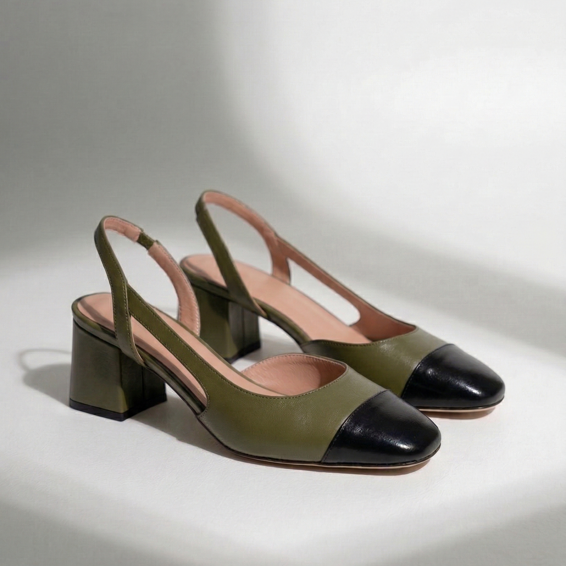 Pair of green and black cap-toe slingback heels on a light gray background