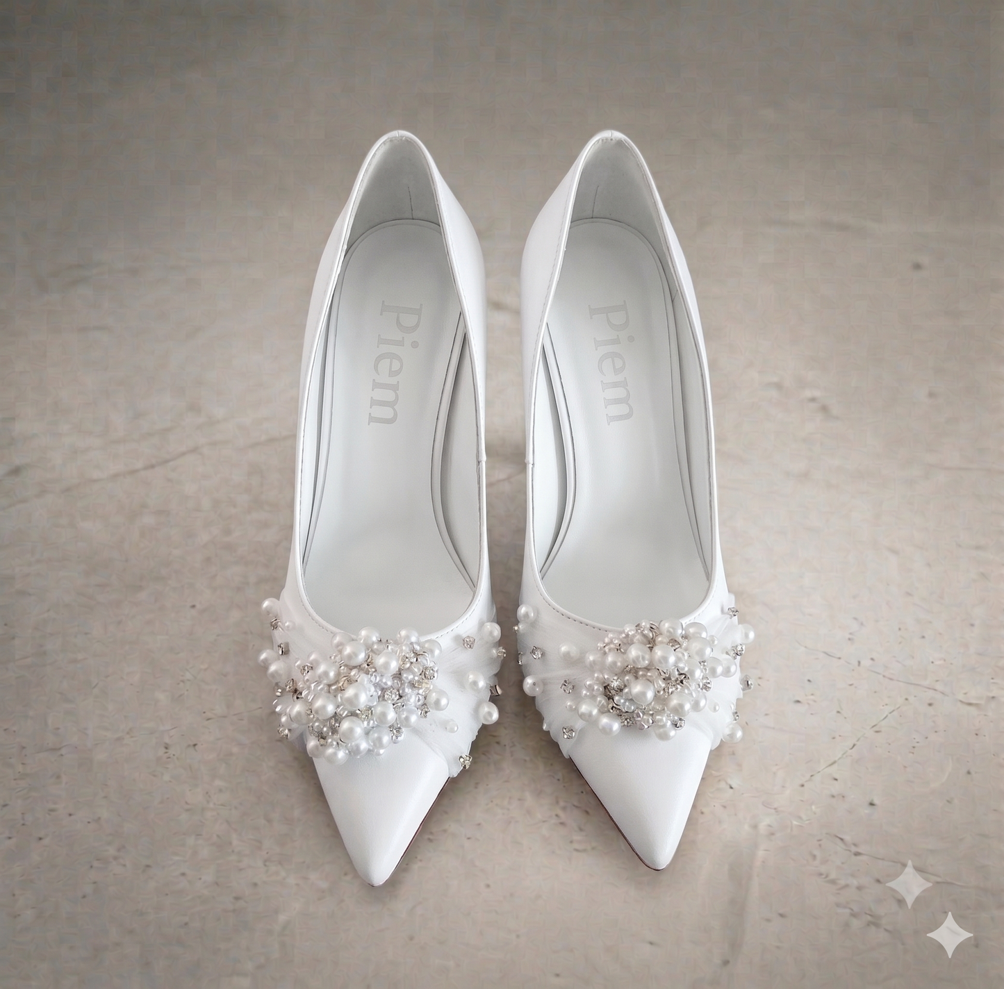 White high-heeled shoes with pearl embellishments on a neutral background