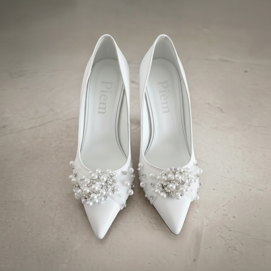 White high-heeled shoes with pearl embellishments on a neutral background