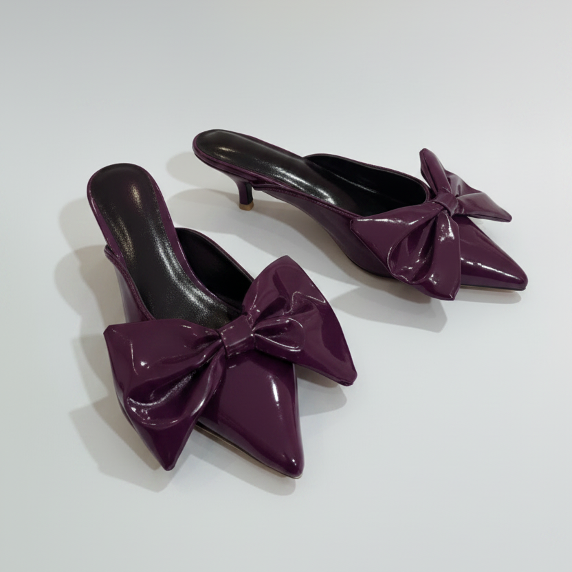 Black patent leather high heels with bow details on a white background