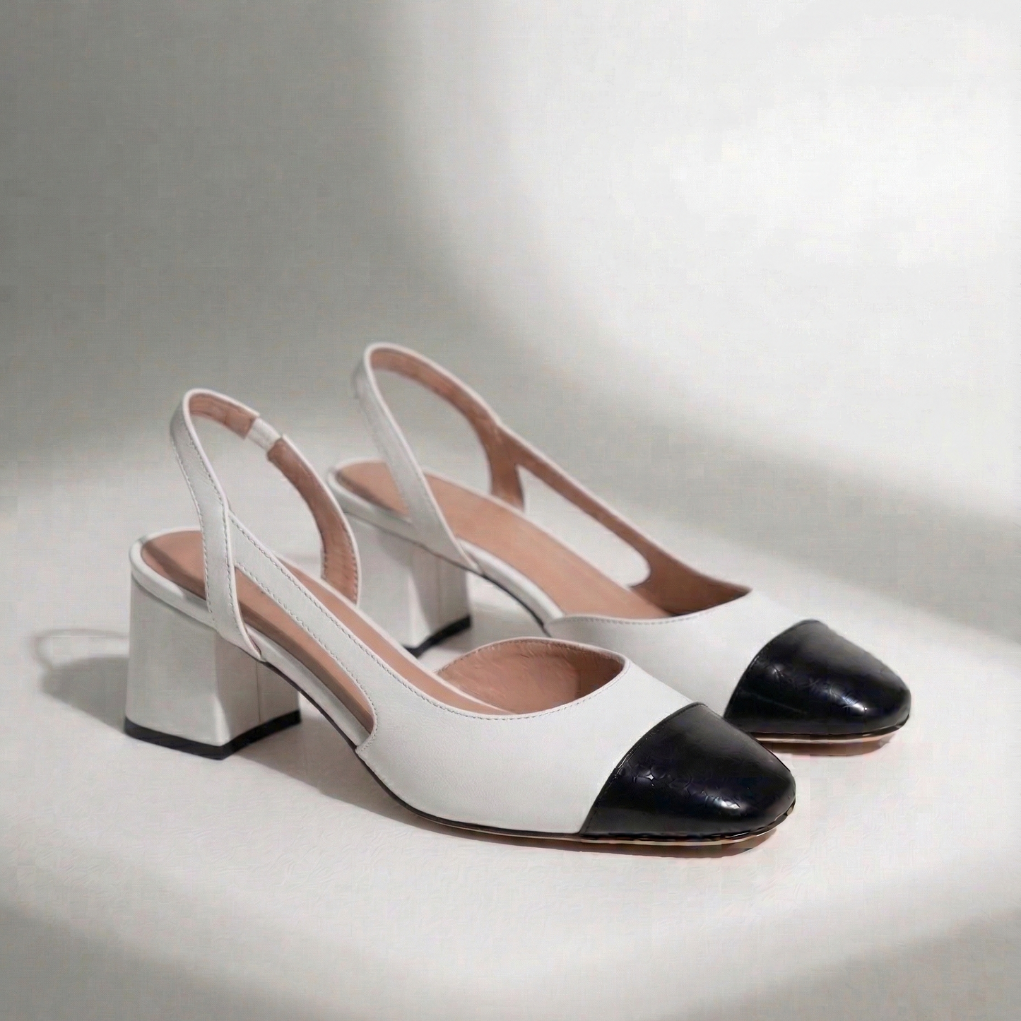 White high-heeled shoes with black cap-toe on a light gray background