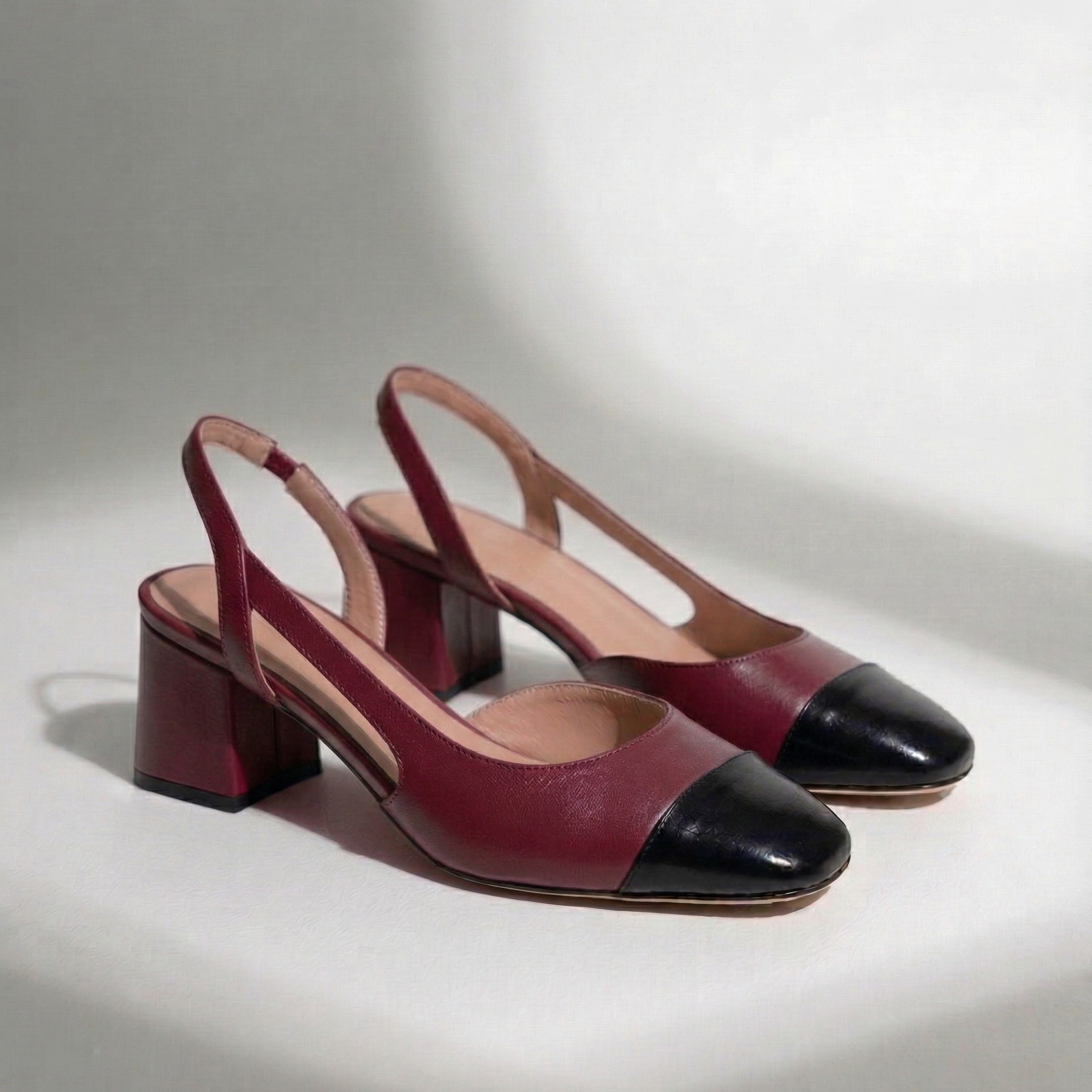 Pair of maroon and black high-heeled shoes on a light gray background