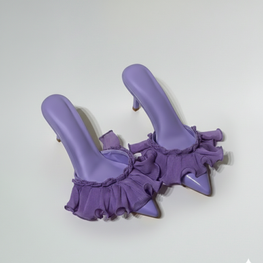 Pair of purple high-heeled shoes with ruffled details on a light gray background