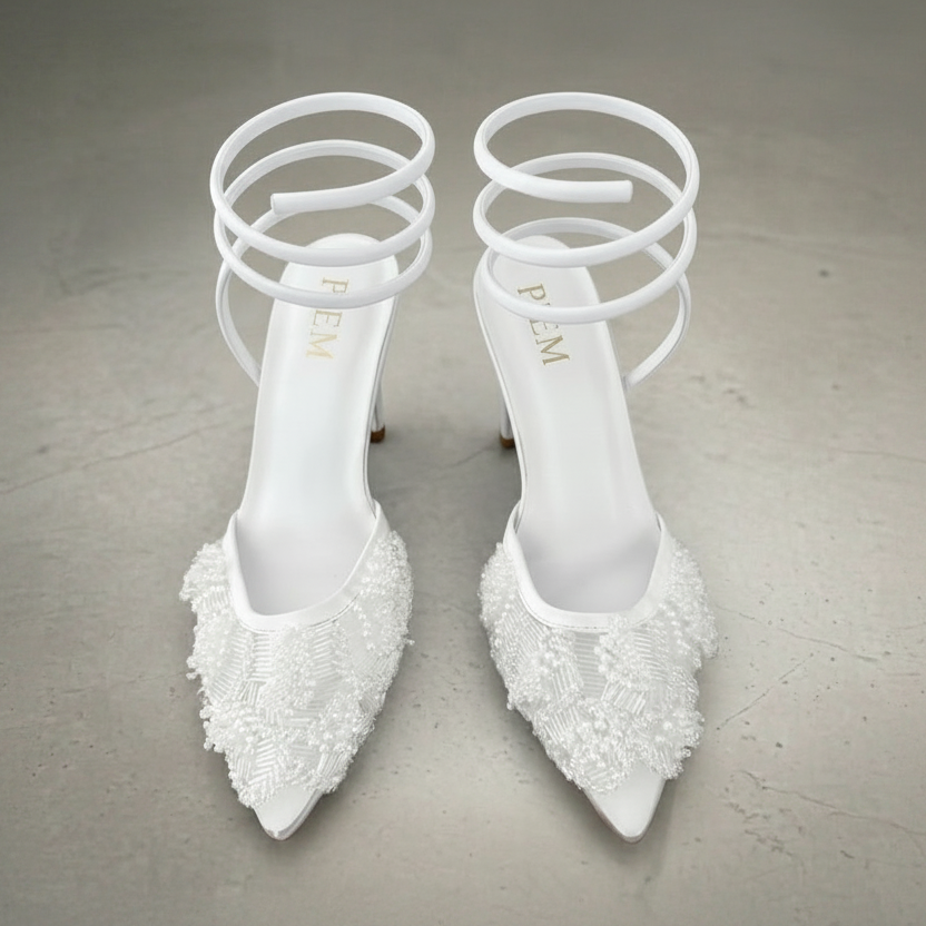 Pair of white high-heeled shoes with decorative elements on a gray background