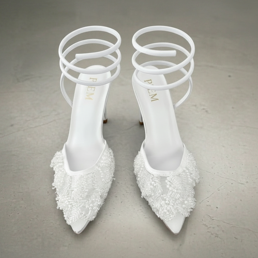 Pair of white high-heeled shoes with decorative elements on a gray background