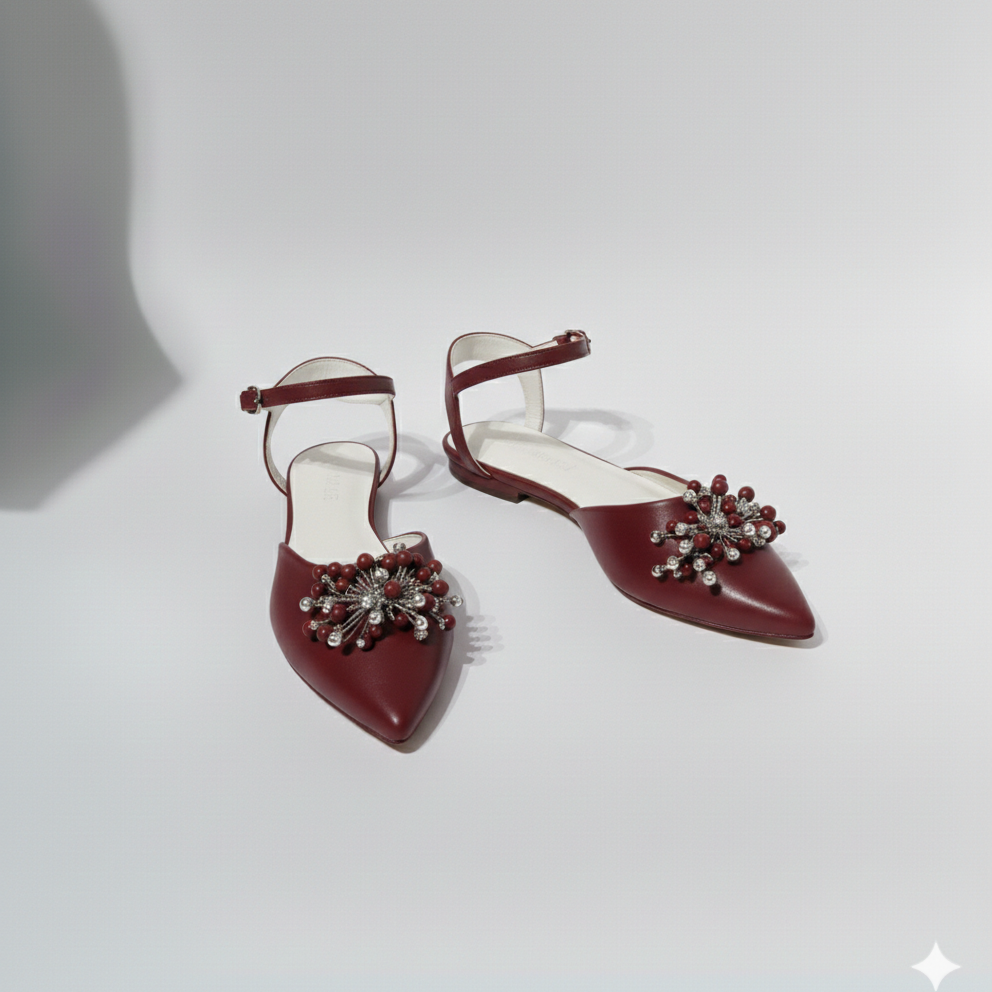 Pair of maroon shoes with decorative embellishments on a light gray background